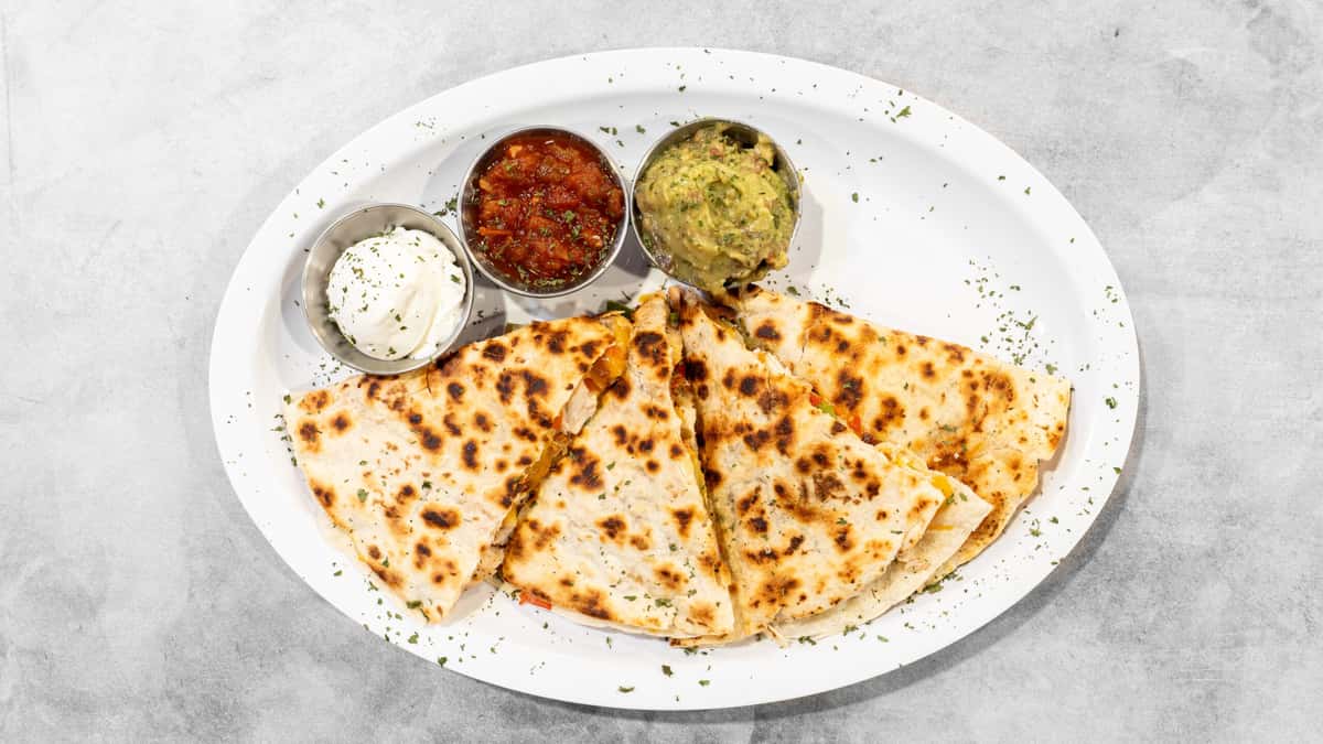 Coaches Corner's golden-brown quesadilla triangles are served on a white platter with vibrant red salsa, fresh green guacamole, and creamy white sour cream.