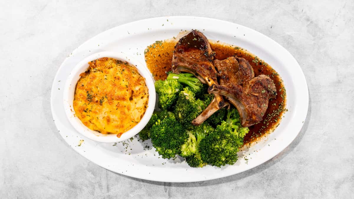 Coaches Corner's seared lamb chops, vibrant green broccoli, and golden baked mac & cheese on a white plate.