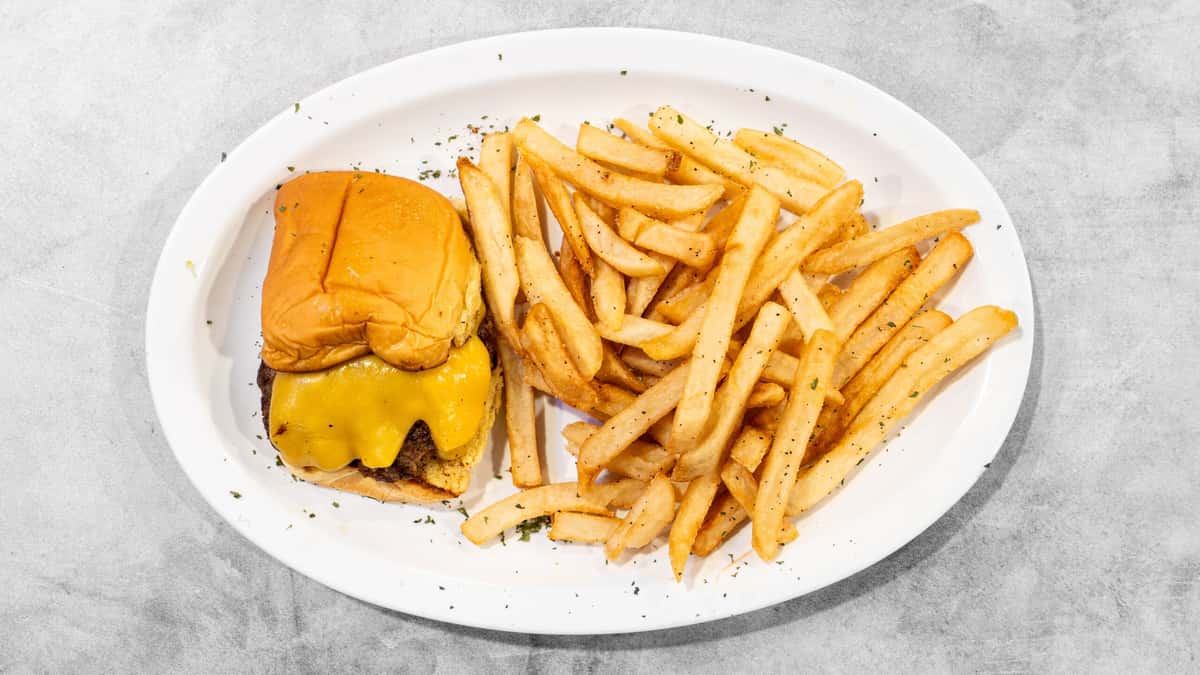 Coaches Corner cheeseburger with melted yellow cheese and golden french fries served on a white plate.