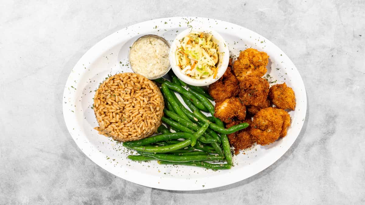 Coaches Corner's golden fried shrimp, vibrant green beans, and seasoned brown rice, served with creamy coleslaw and tartar sauce on a white plate.
