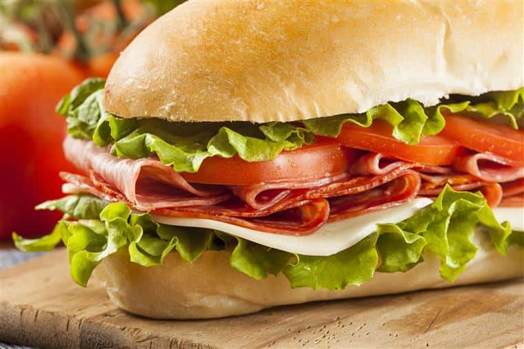 Homemade Italian Sub Sandwich with Salami, Tomato, and Lettuce with toamtoes on the vine blurred in the background