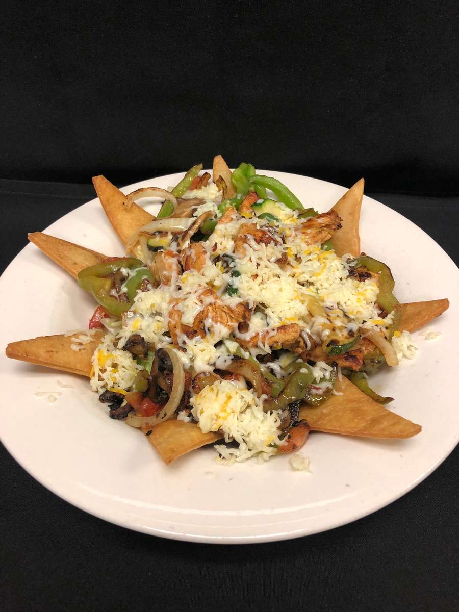 Grilled chicken fajitas over a bed of lettuce topped with flour chips and sprinkled with cheese