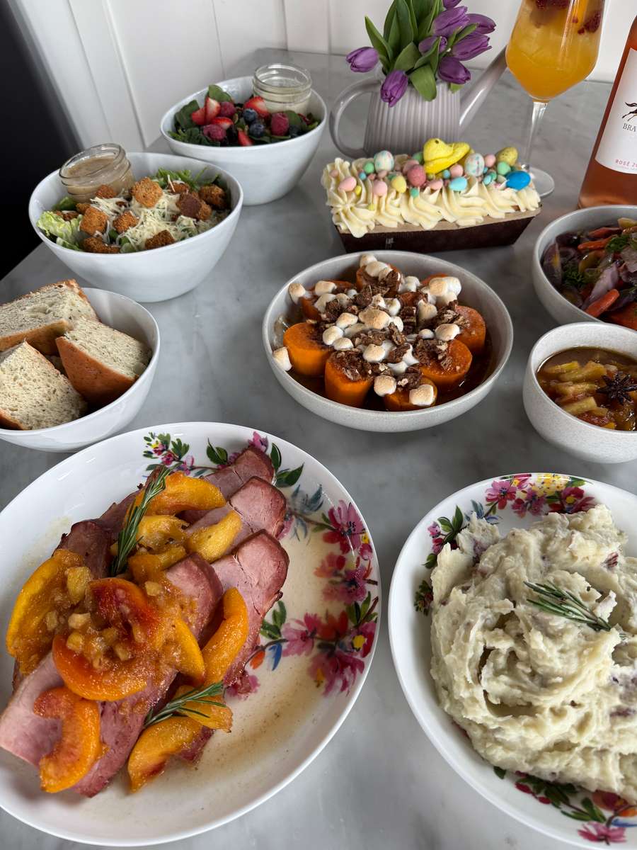 Easter brunch spread with glazed ham, mashed potatoes, roasted carrots with marshmallows, fresh salads, bread, and festive dessert on a bright restaurant table