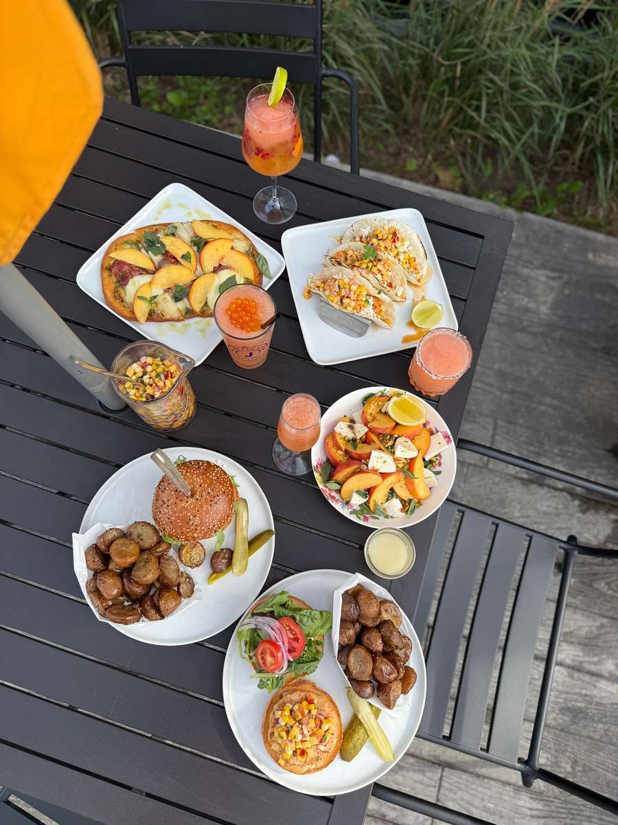 outdoor dining table with gourmet burgers, tacos, flatbread pizza, roasted potatoes, and colorful cocktails at a casual patio restaurant