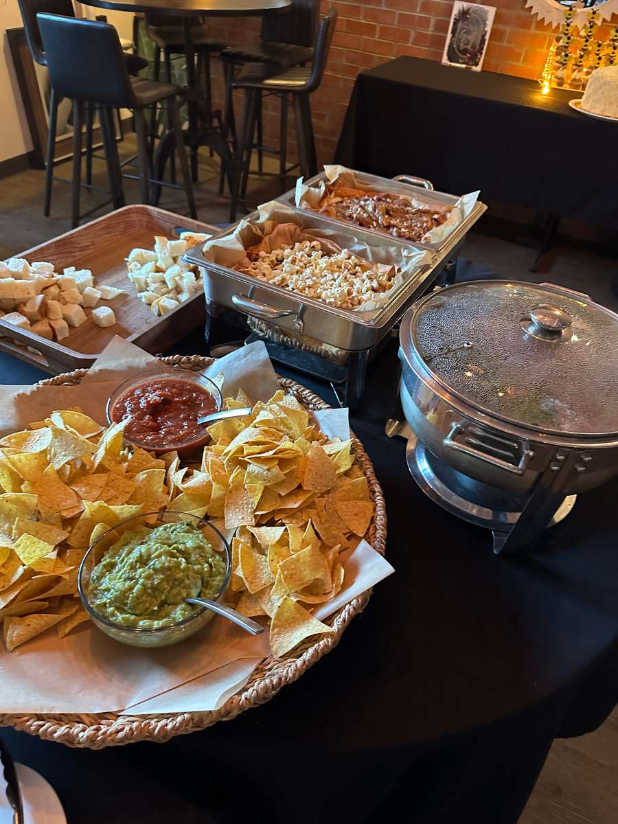 Buffet spread with tortilla chips, fresh guacamole and salsa, queso dip, mac and cheese, and bread cubes in a casual restaurant setting