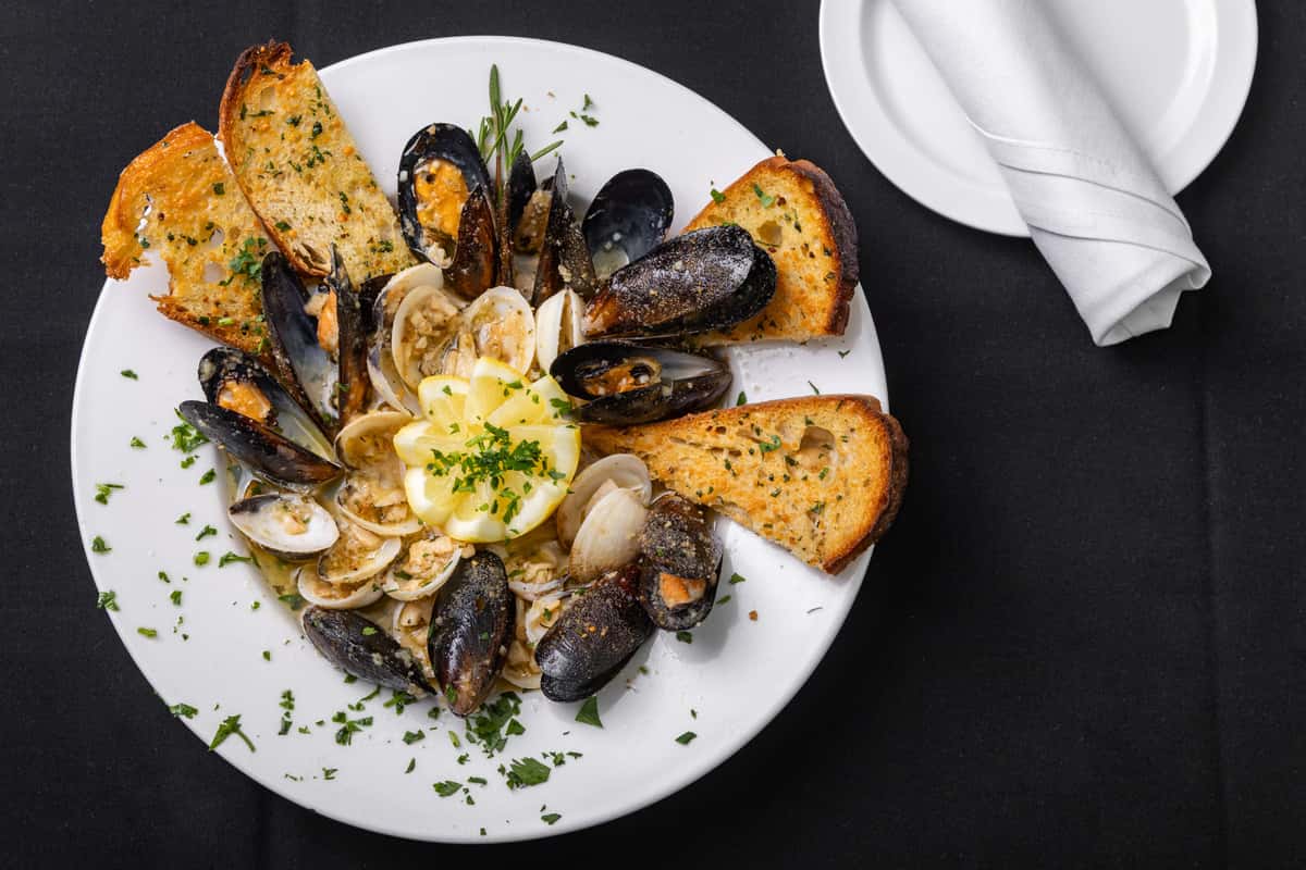 Steamed mussels and clams in garlic butter, plated with toasted garlic bread and lemon wedges on a white plate.