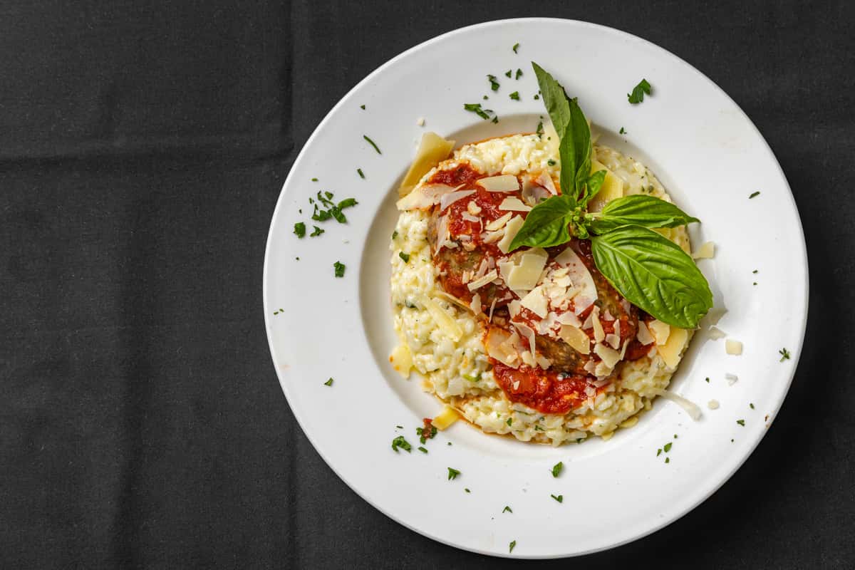 Italian-style meatballs in marinara sauce served on a bed of cheesy risotto, garnished with shaved Parmesan and basil.