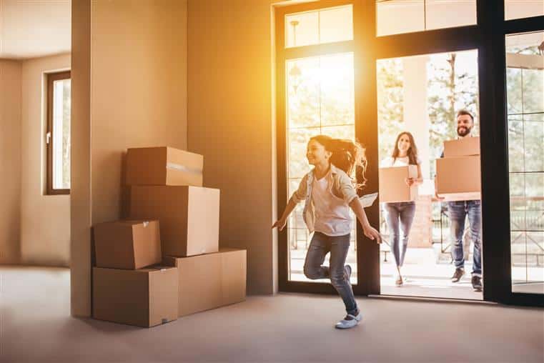 a stack of boxes against the wall with a small child running in the room in front of her parents