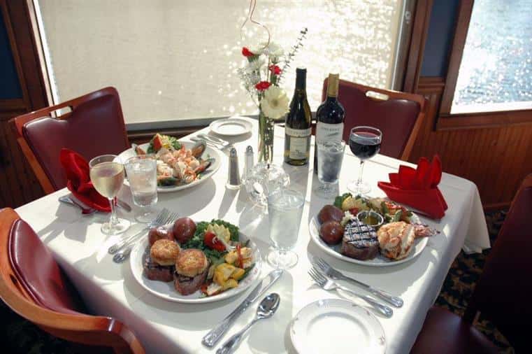 table with various plates of food such as fish, burgers, mussels and two bottles of wine