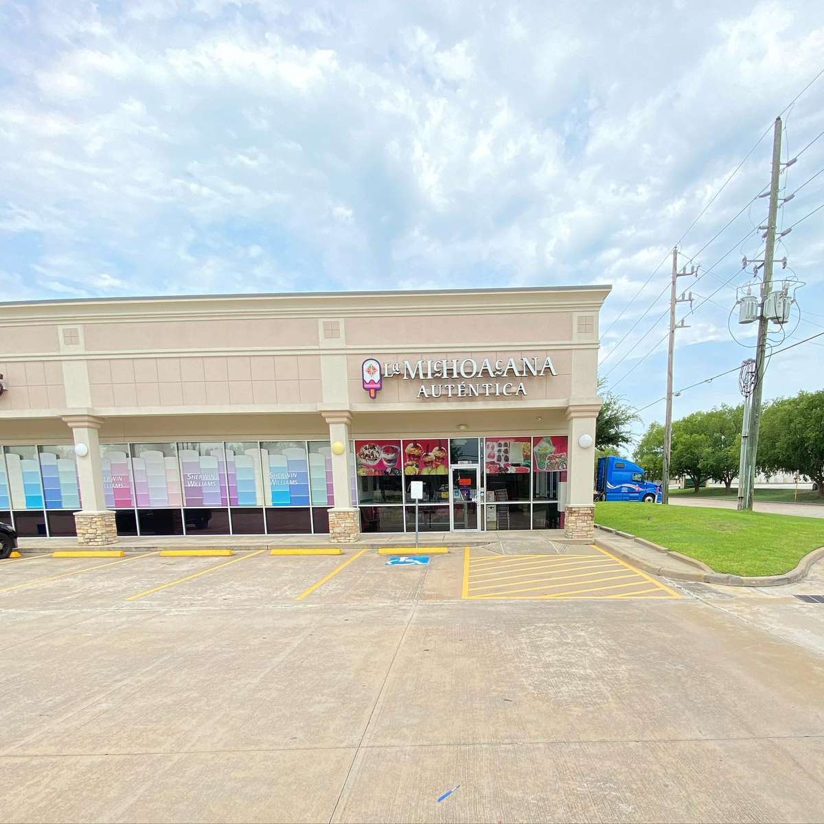 A storefront of "La Michoacana Autentica" with a clear sky, visible parking spaces, and large windows displaying colorful posters.