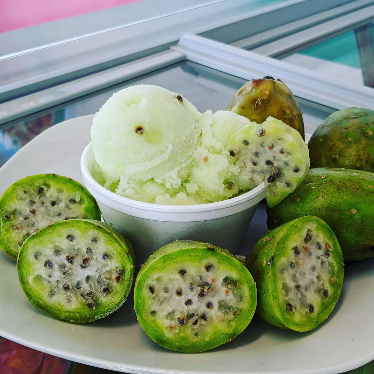 A bowl of prickly pear (sabra) sorbet surrounded by fresh, halved prickly pears with visible seeds.