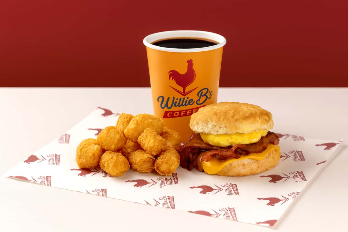 Willie B's Chicken Coupe breakfast meal featuring a biscuit sandwich, crispy tater tots, and branded coffee against a vibrant red backdrop.