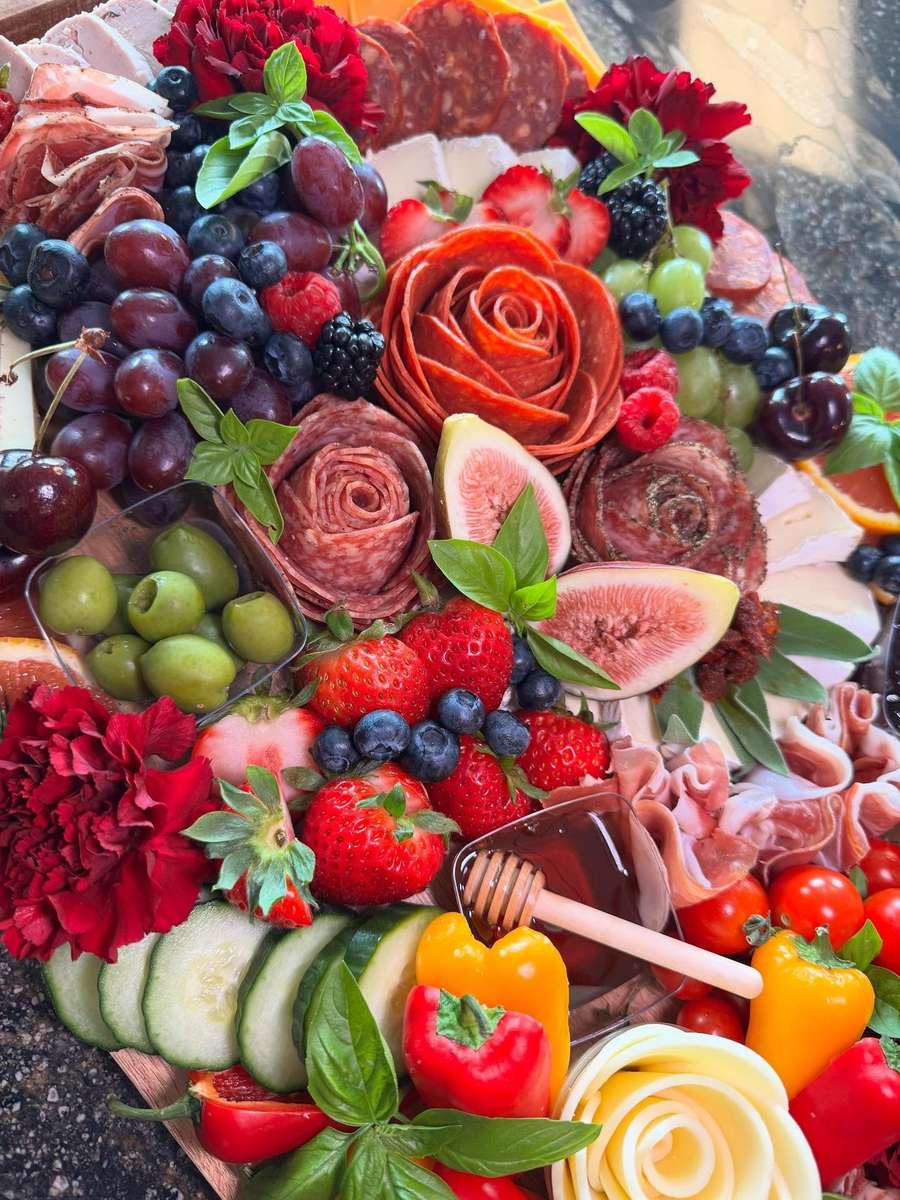 Elegant charcuterie platter with salami roses, figs, strawberries, olives, fresh vegetables, and soft cheeses, artistically styled with edible flowers and basil.