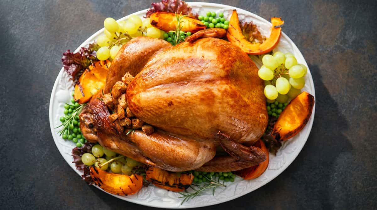 Roasted whole turkey on a white platter, garnished with green grapes, peas, roasted pumpkin, and rosemary.