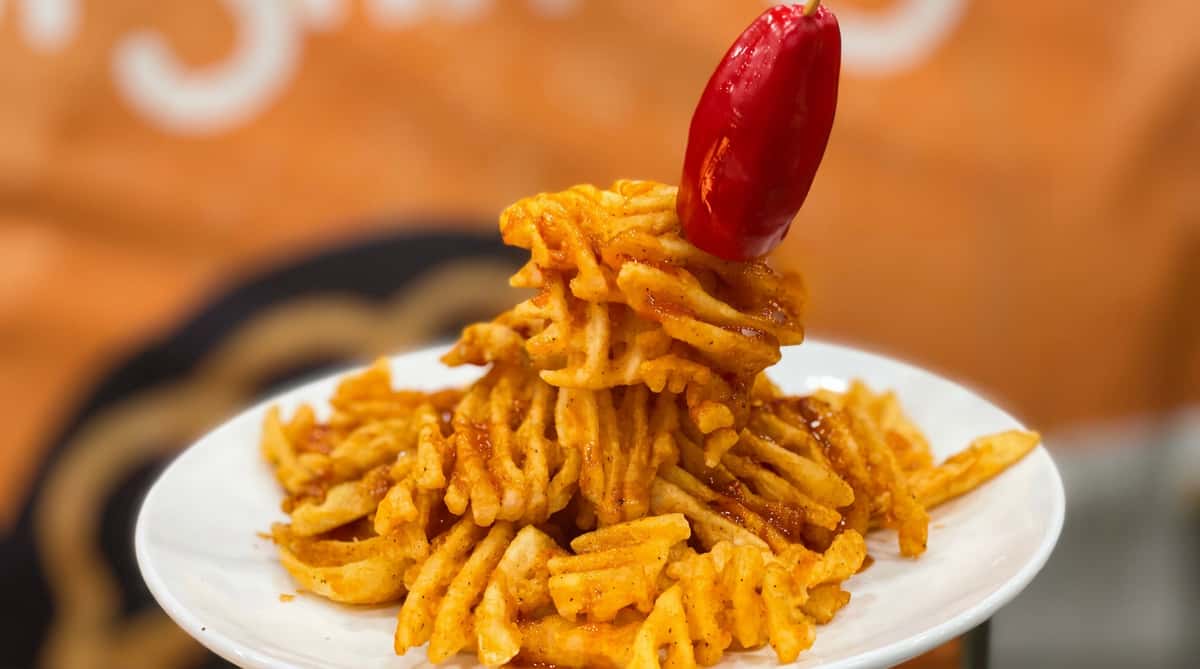 Crispy waffle fries piled high and seasoned with bold spices, topped with a bright red pepper for a playful appetizer presentation.