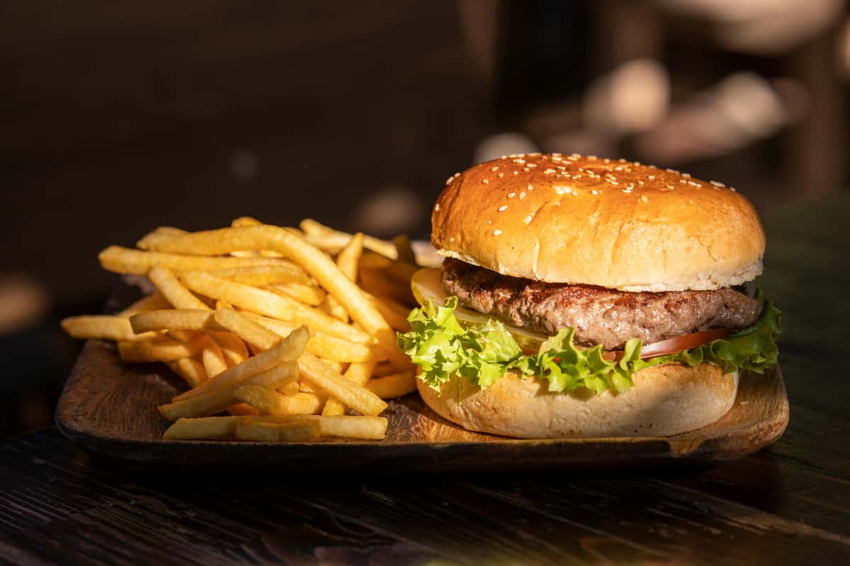 Classic cheeseburger with lettuce and tomato served with golden fries on a wooden board