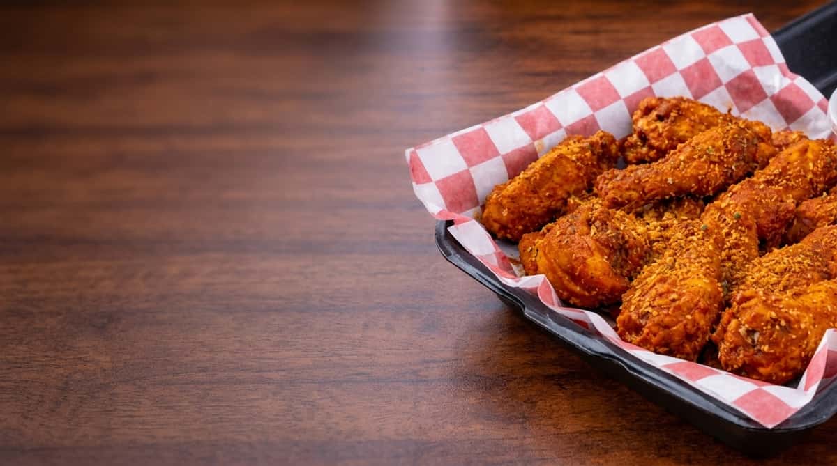 Basket of crispy dry rub chicken wings on red checkered deli paper.