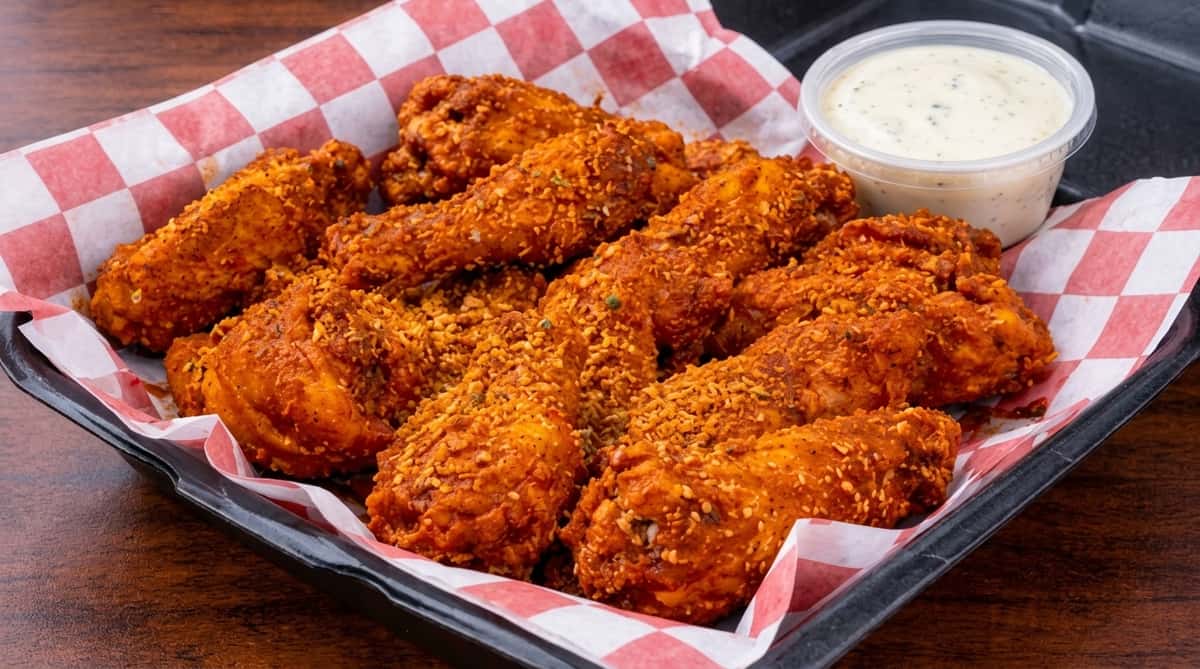 Dry rub chicken wings served in a basket with ranch dipping sauce on red checkered deli paper.