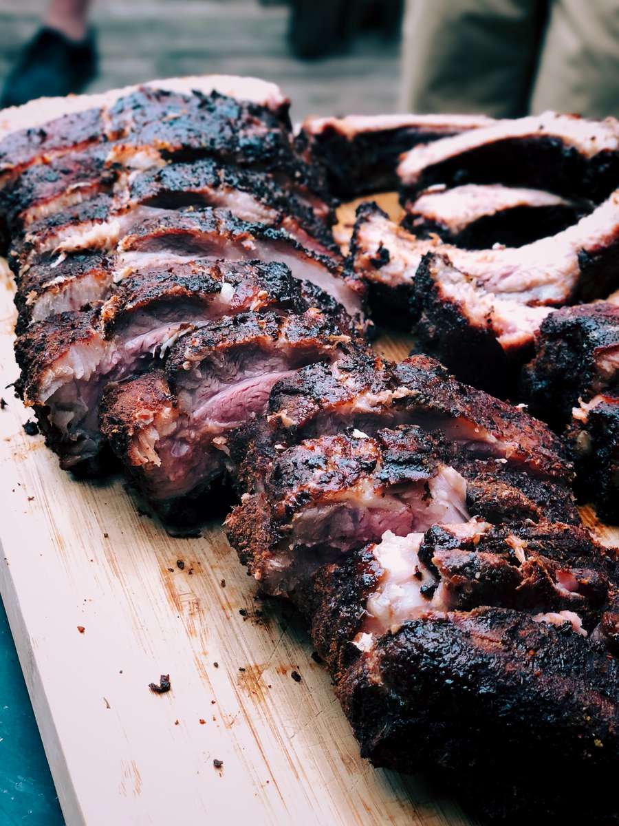 Sliced smoked BBQ brisket with a dark, caramelized crust and juicy, tender meat served on a wooden cutting board.