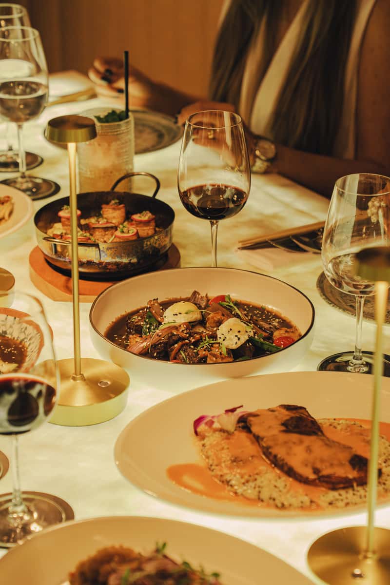 Table spread of a variety of meals with warm lighting and drinks
