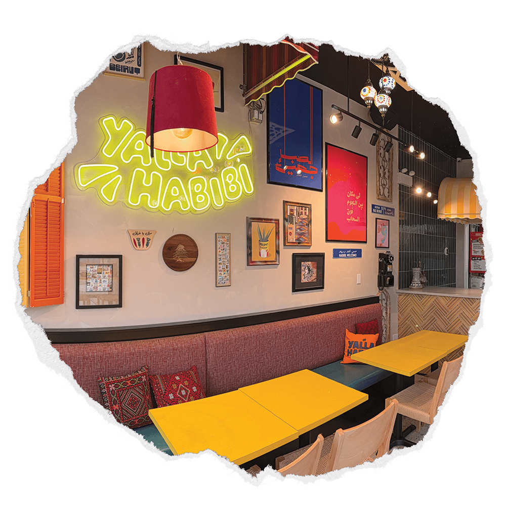Cozy interior of Habibi's Chicken & Falafel with neon "Yalla Habibi" sign, colorful Middle Eastern decor, and casual dining seating with bright tables and patterned cushions