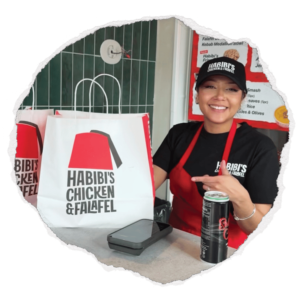 Employee standing with a Habibi's takeout bag sitting on a counter