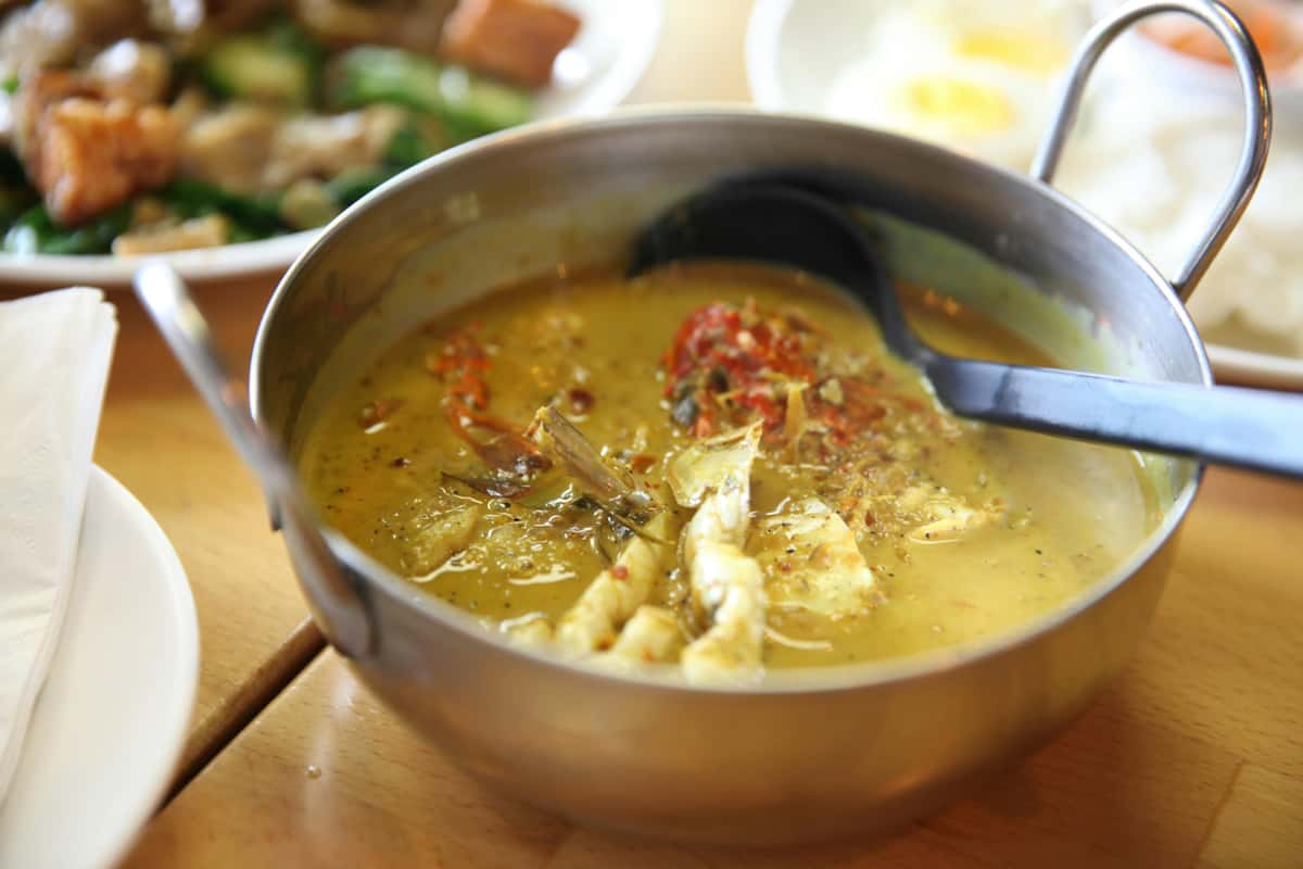 A close-up of a flavorful Thai chicken curry served in a metal bowl with fresh herbs.