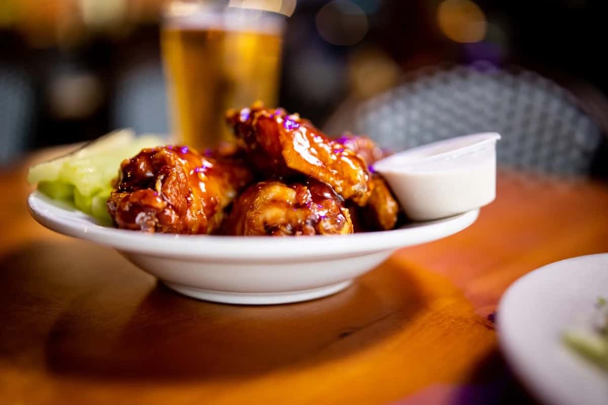 A plate of saucy buffalo wings served with crisp celery sticks and a side of ranch dressing, perfect alongside a cold beer.