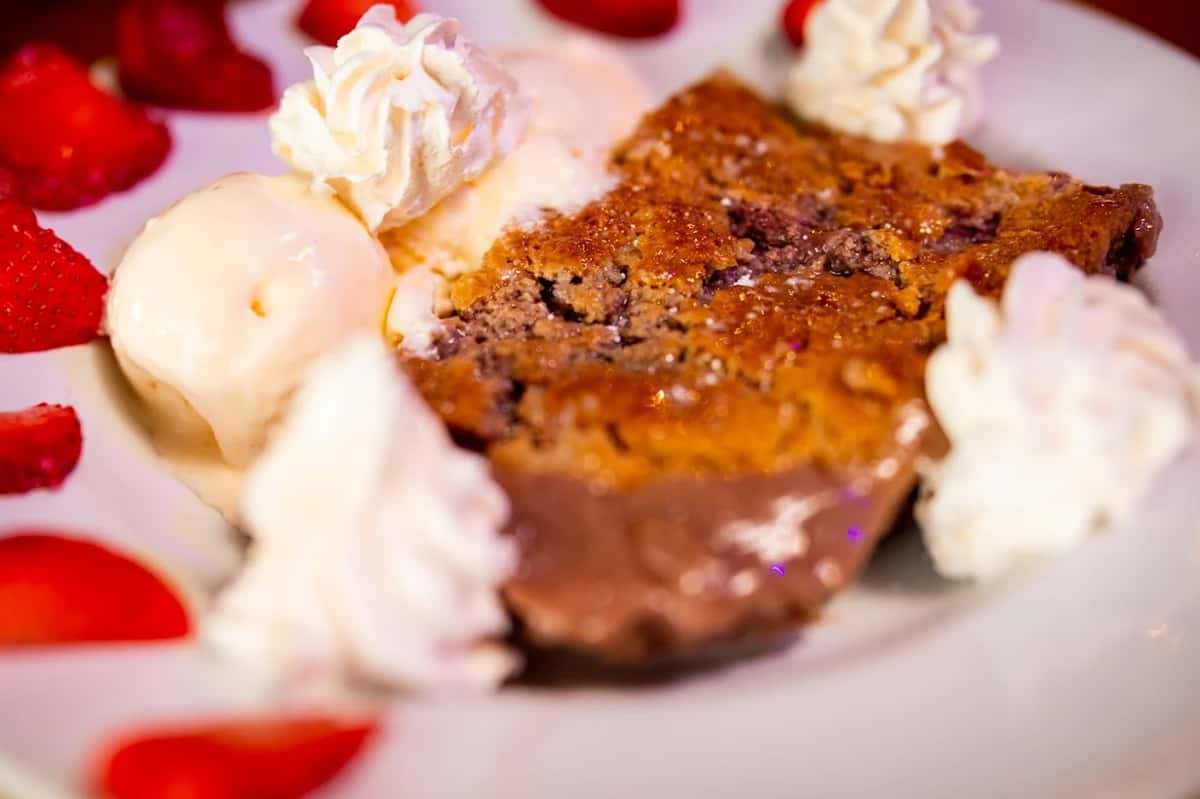 Warm berry cobbler served with scoops of vanilla ice cream, whipped cream, and fresh sliced strawberries.