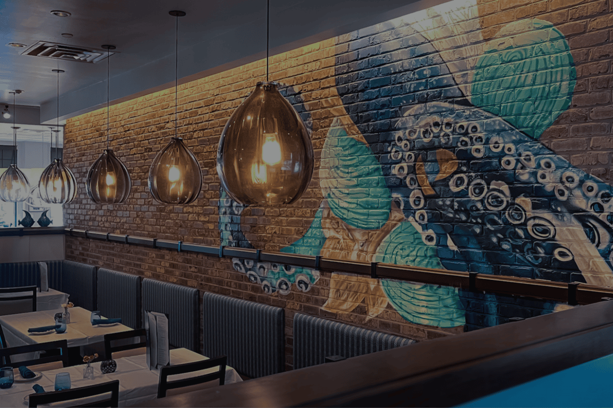 Osteria's main dining room features a hand-painted octopus mural on exposed brick, surrounded by pendant lighting and stylish banquette seating. A visual anchor for the restaurant's coastal-meets-industrial aesthetic.