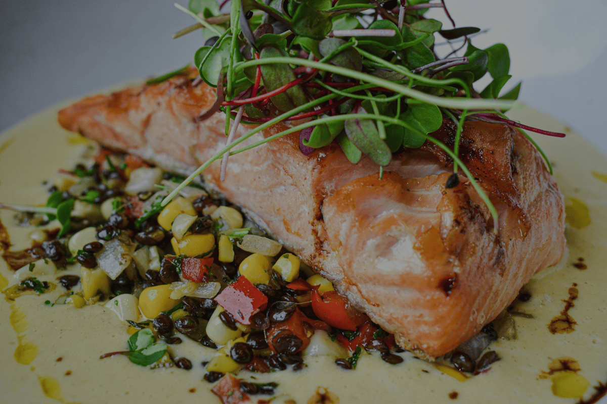 Pan-seared salmon served over sweet corn succotash, lentils, and a creamy lemon beurre blanc—topped with microgreens for a fresh coastal finish.