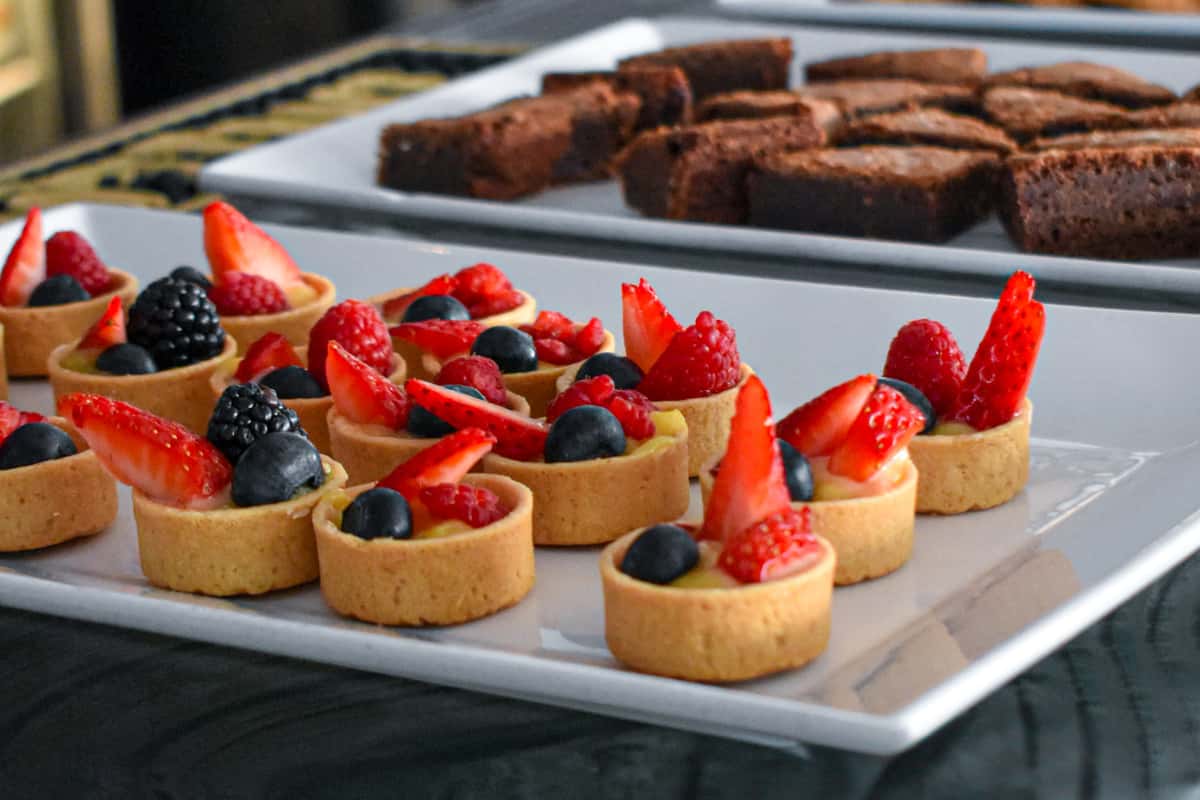 Fresh-baked mini fruit tarts filled with pastry cream and topped with berries, served alongside rich chocolate brownie bites—perfect for private events and catering spreads at Osteria.