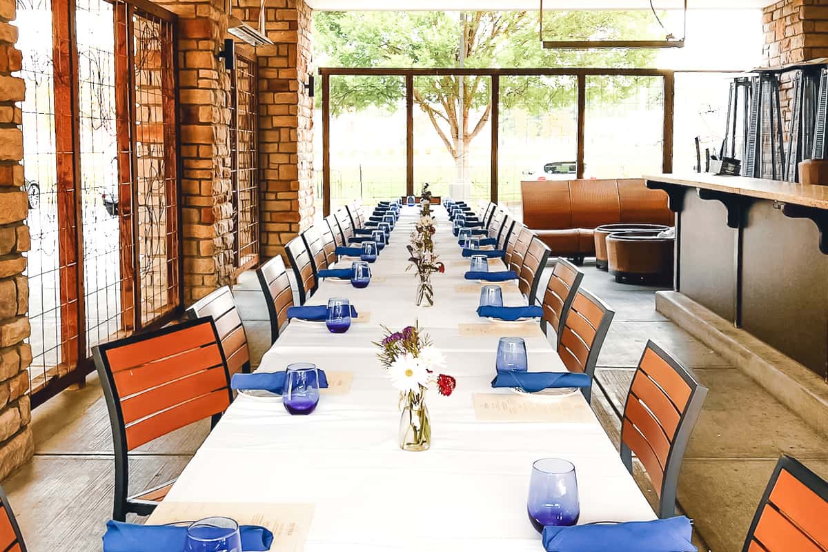 Long private dining table setup on Osteria's enclosed patio with white linens and blue glasses