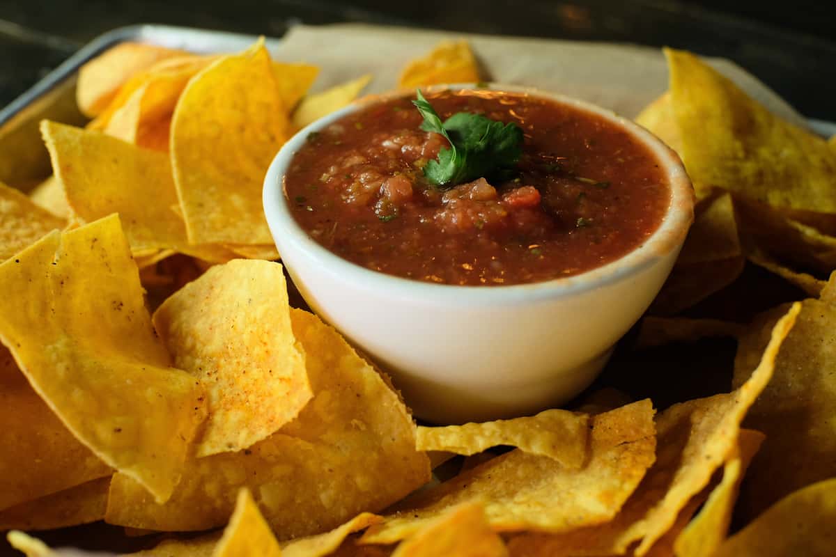 Crispy tortilla chips served with a bowl of chunky salsa topped with fresh cilantro on a parchment-lined tray.