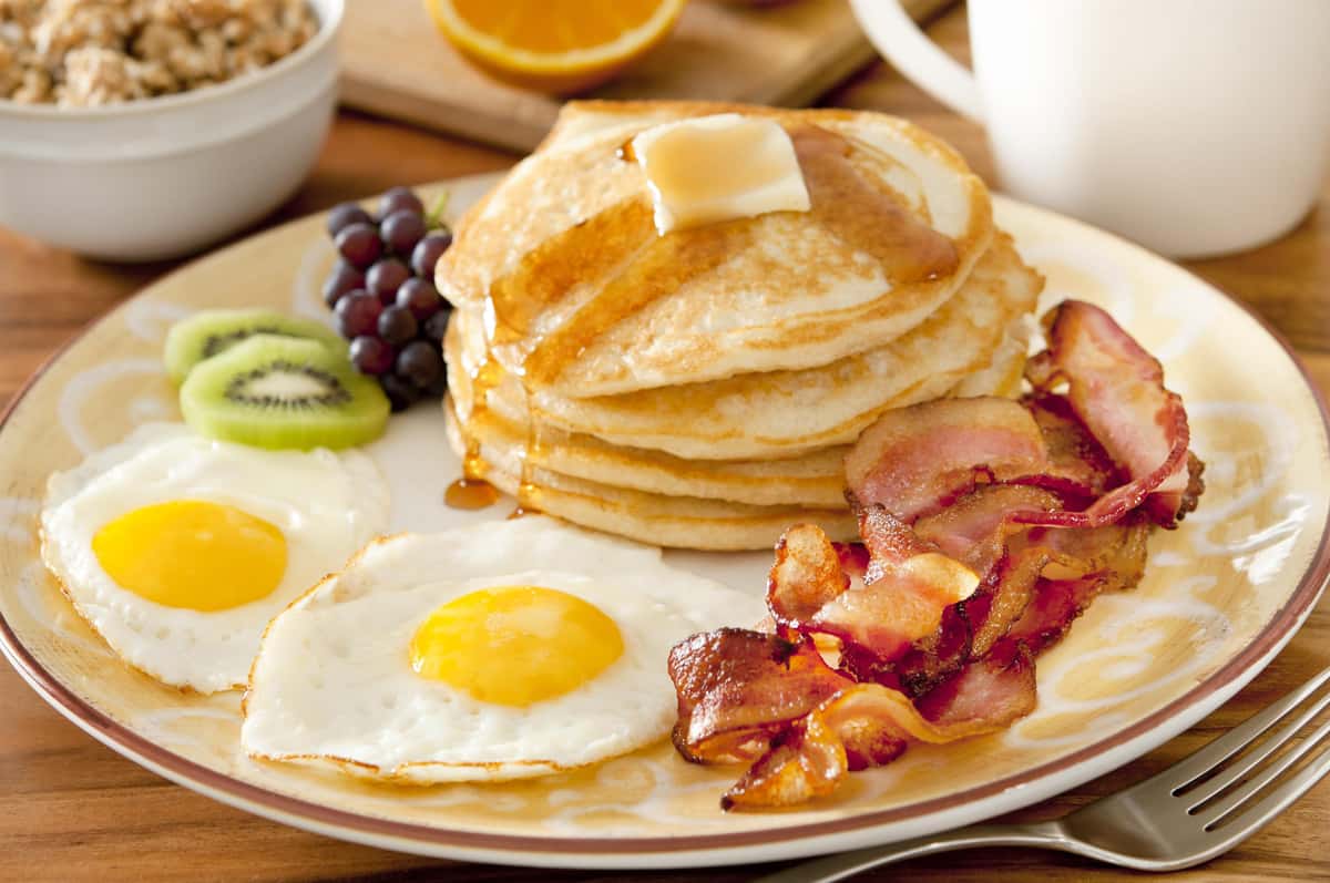 Closeup of a breakfast plate with pancakes, eggs, bacon and fruit