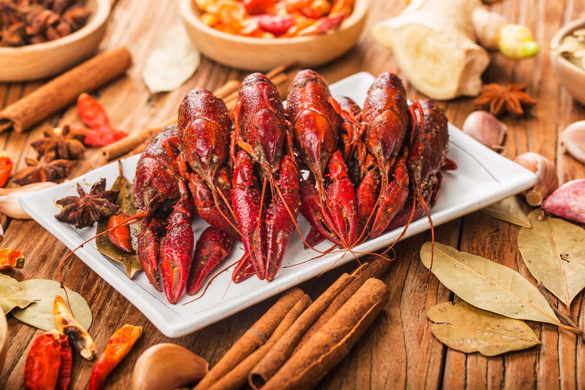 Plate of boiled crawfish with spices and herbs on a wooden table.