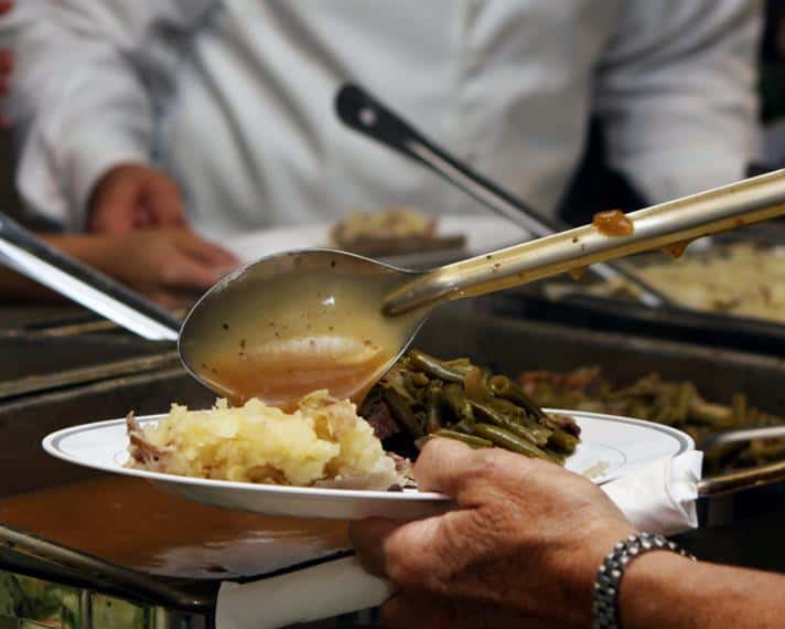 Person self-serving mashed potatoes and green beans at food station with sternos.