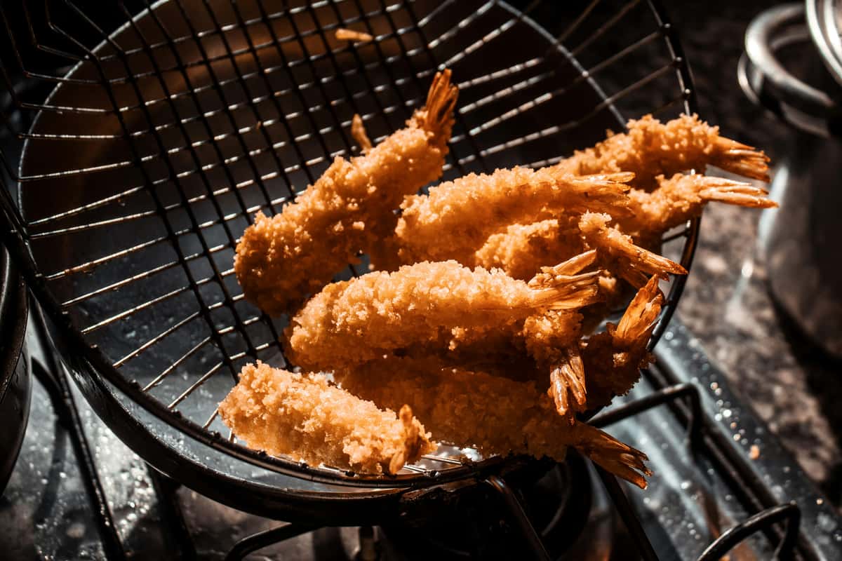 Crispy breaded fried shrimp draining in fryer basket, golden seafood appetizer with crunchy coating