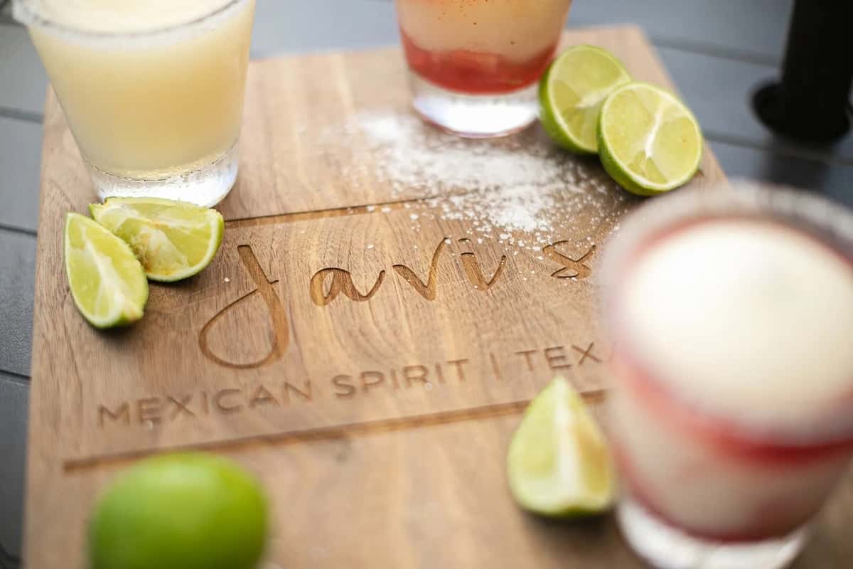 Assorted margaritas with lime wedges and salt on branded wooden board, Mexican restaurant drink display