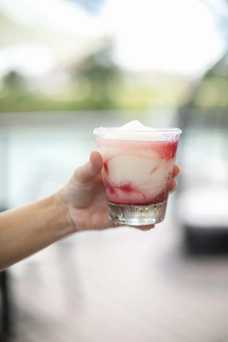 Hand holding creamy strawberry margarita with salted rim, refreshing summer cocktail