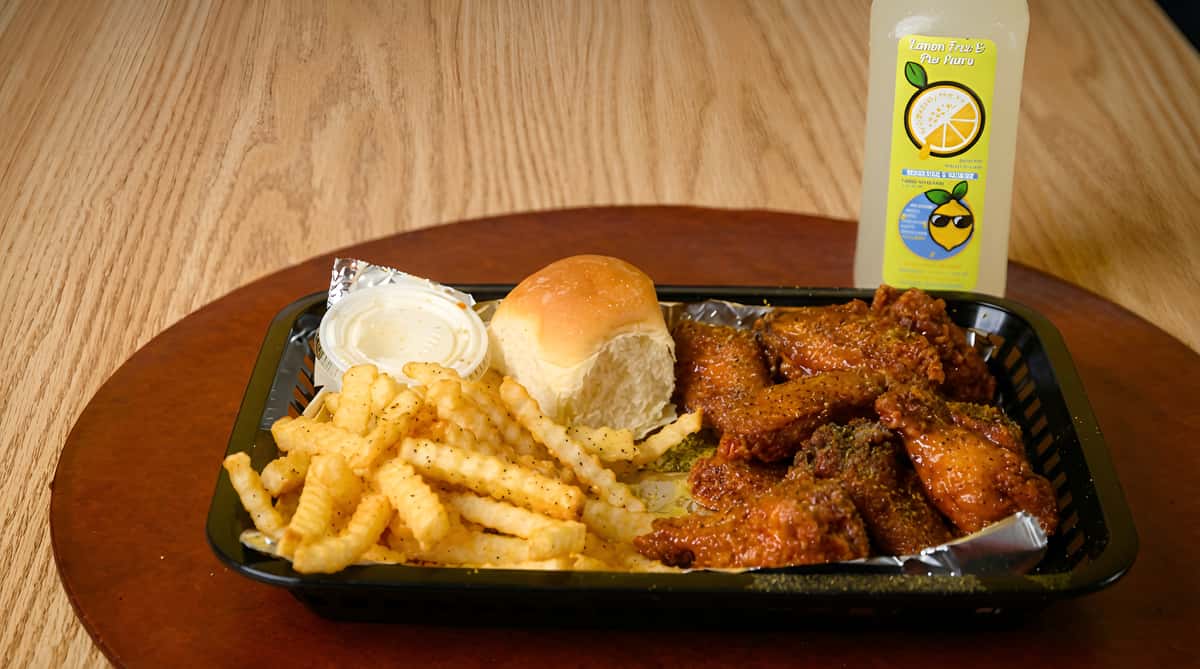 Chicken wing meal with crinkle fries, a bread roll, sauce cup, and lemonade bottle on a black tray.