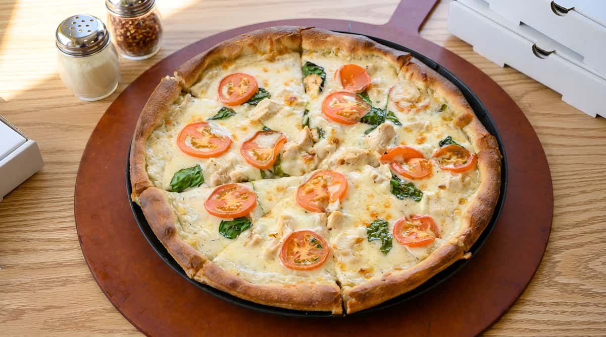 Chicken alfredo pizza with sliced tomatoes and spinach on a wooden board.