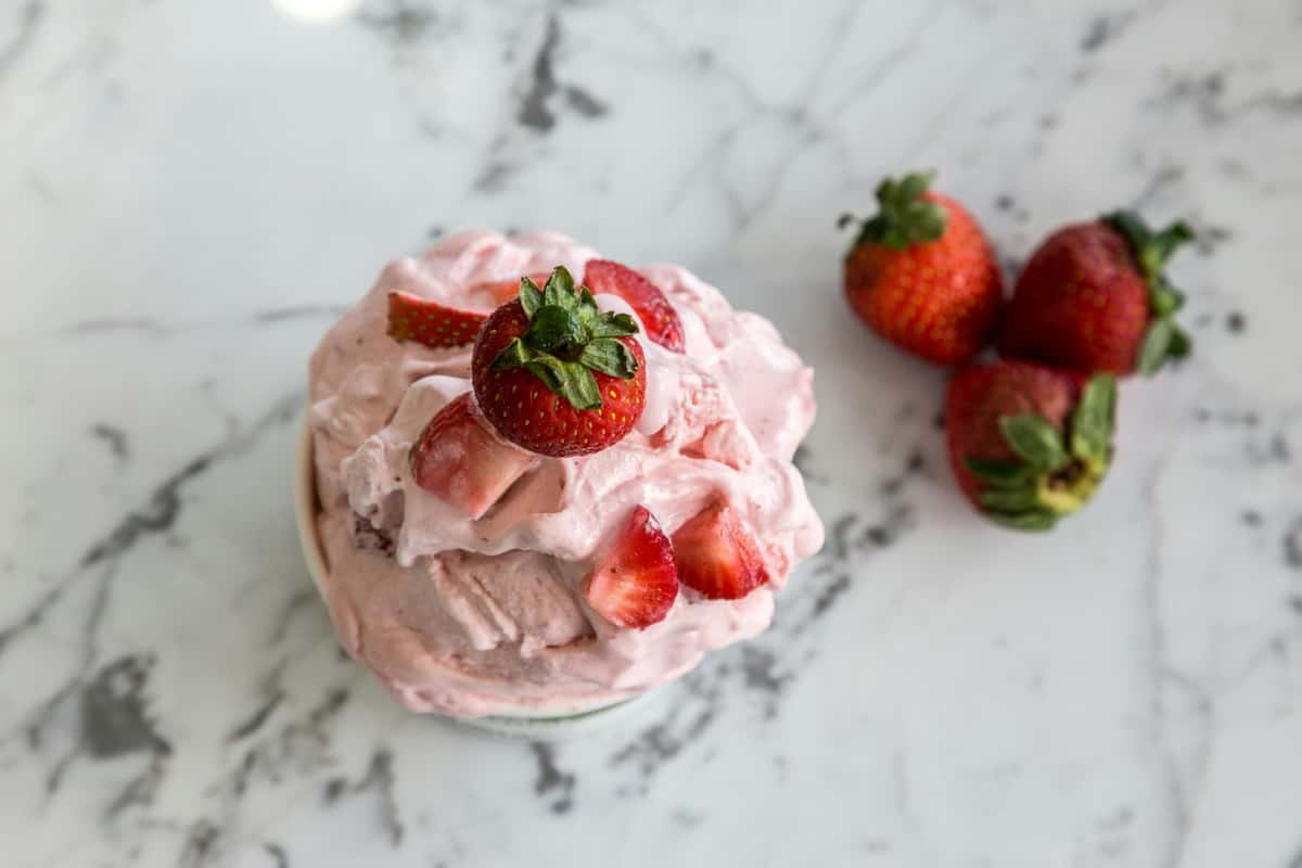Frozen Fusion's creamy pink strawberry dessert, topped with fresh whole and sliced berries on a white marble surface.