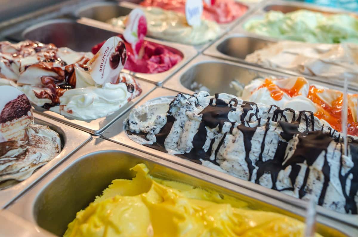 A vibrant display of assorted creamy gelato flavors, including bright yellow, chocolate-drizzled, and cherry swirl, at Frozen Fusion.