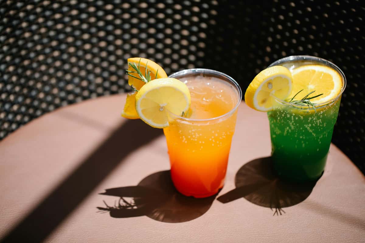 Vibrant orange and green cocktails garnished with lemon slices and rosemary in plastic cups.