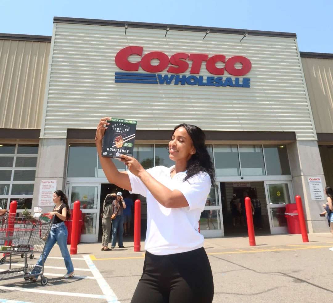 Woman holding a box of Brooklyn Dumpling Shop dumplings in front of a Costco location