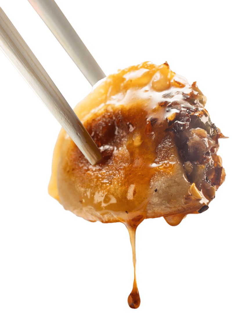 Chopsticks holding a dumpling dripping with sauce