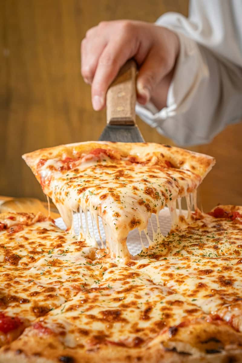 Hand lifting a slice of hot, cheesy pizza with golden-brown crust and melted mozzarella, perfect for Italian restaurant menus or delivery ads.