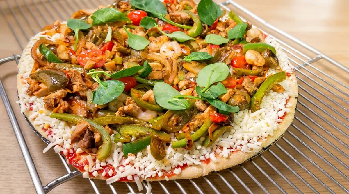 Unbaked pizza with tomato sauce, mozzarella, peppers, onions, chicken, shrimp, cherry tomatoes, and spinach.