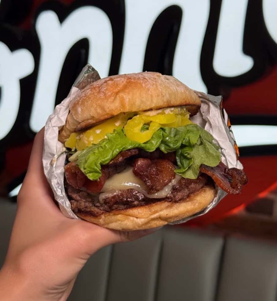 Holding up a burger in front of Fat Ronnie's sign